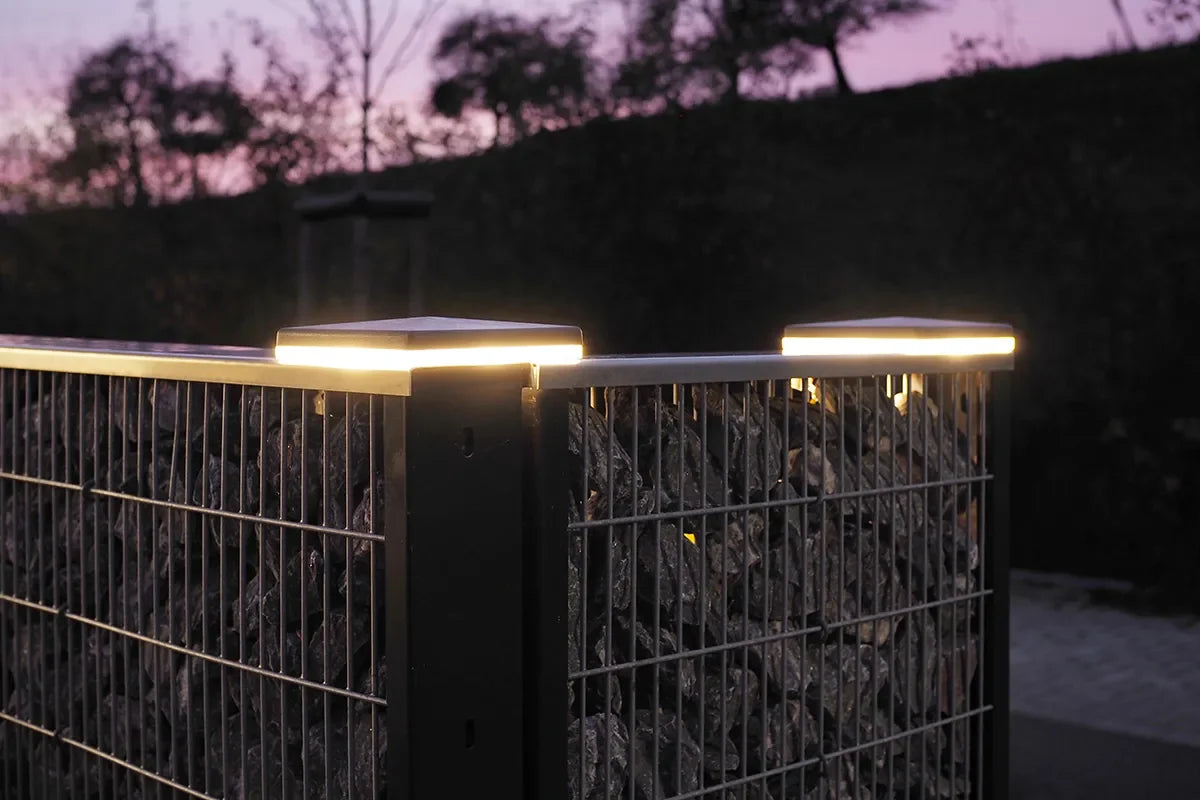Zaunbeleuchtung mit LED-Pfostenkappen an einem Gabionenzaun in der Dämmerung