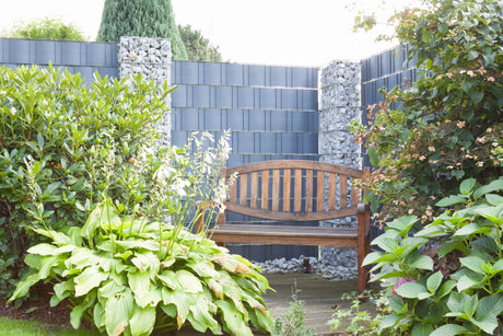 Gabionensäulen RUBIN mit Sichtschutzzaun hinter einer Gartenbank zwischen Stauden